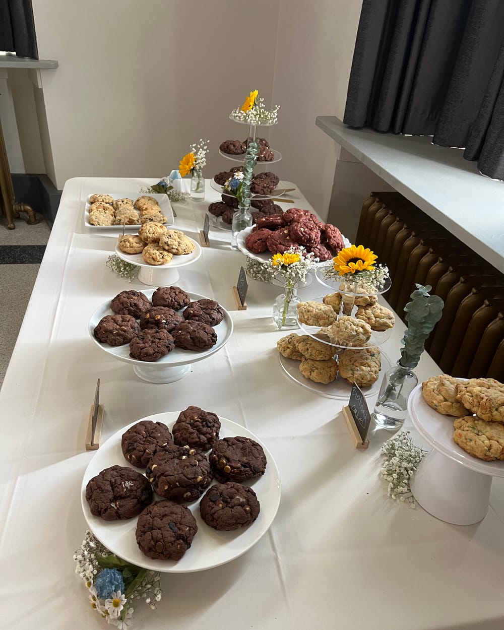 An event dessert table with cookie stands, chalkboard flavour signs and sunflowers